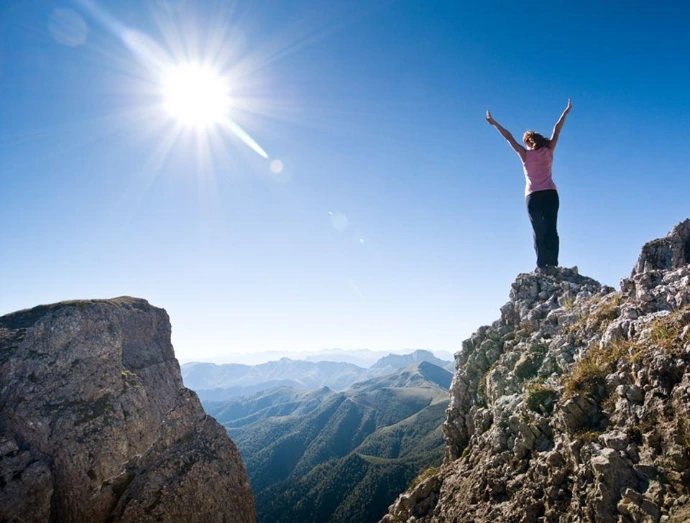 Vrouw met de armen in de lucht op een bergtop in de zon