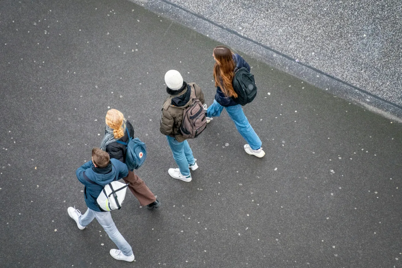 Vier jongeren met een rugzak steken een straat over, van bovenaf gezien