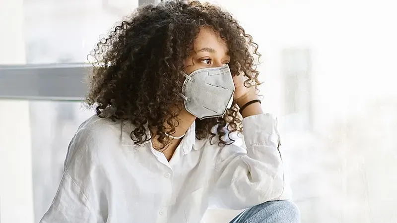 Jonge vrouw met mondmasker kijkt uit het raam